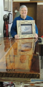 Marie Moran with a table constructed of found material from Grand Junction Main St. buildings, and a piece of a painting by her late son Robert Harper.