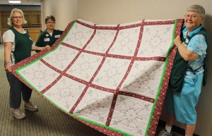 Auxiliary members Judy Larson, Joyce Clark and Elaine Deluhery show off the 2014 quilt currently being raffled as one of many yearly fundraisers.